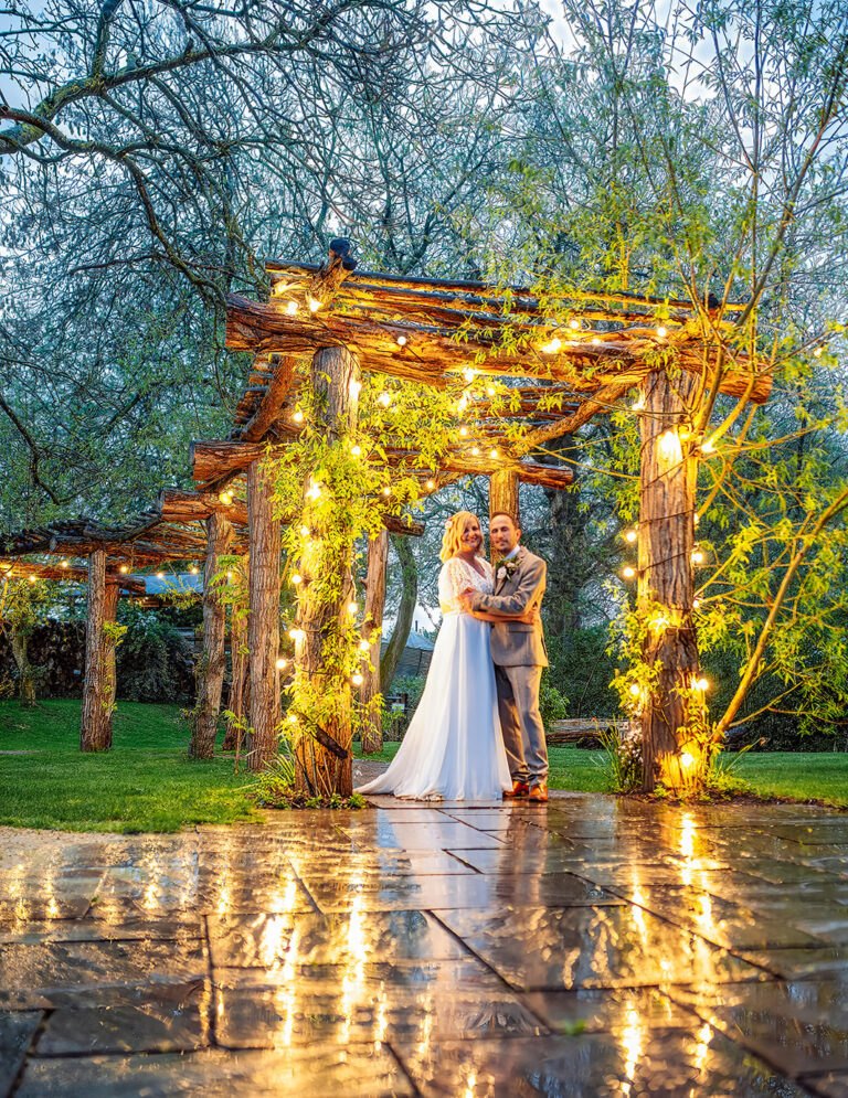 West Midlands wedding venue. Becky & Josh standing under an archway of fairylights strung around a wooden structure