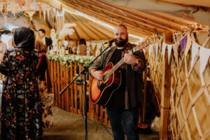 Inside Bennetts Willow Barn's marquee decorated with fairylights bunting and florals, a guitarist plays to guests in front of the bar